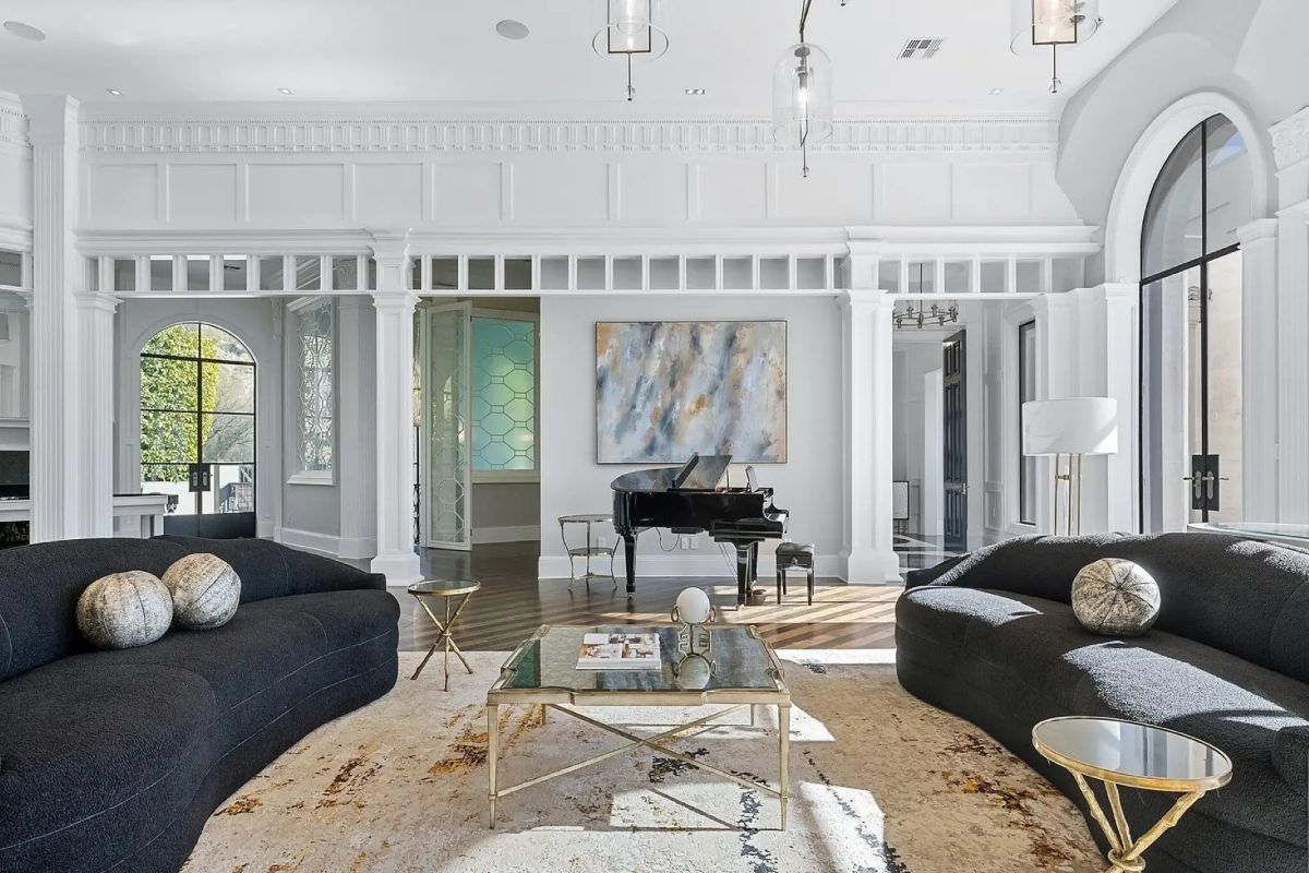 Additional living area view featuring black sofas, baby grand piano, and arched doorway details. 