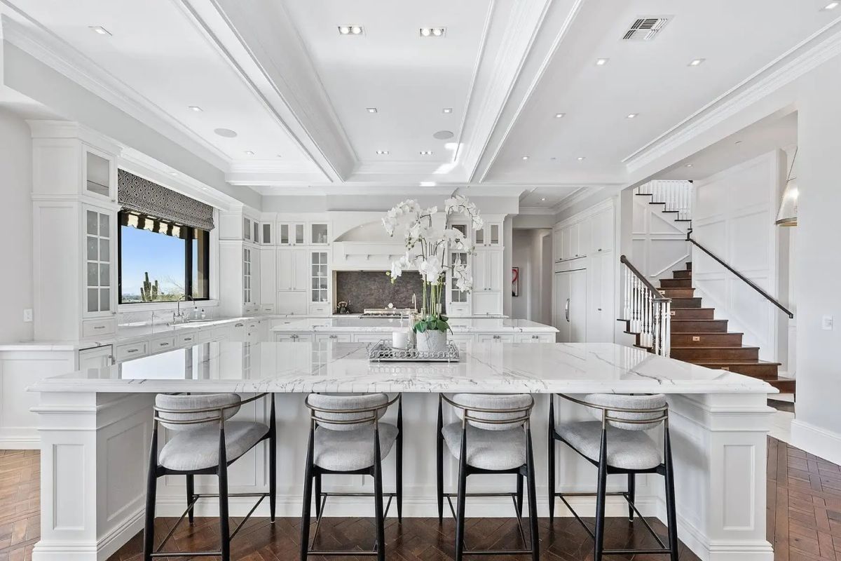 Expansive kitchen with white cabinetry, marble countertops, and oversized center island with seating. 