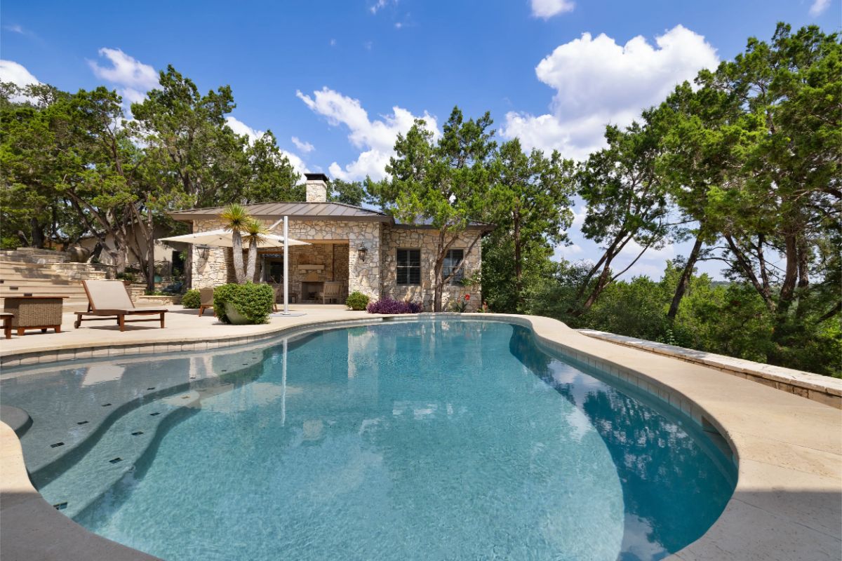 Curved pool with integrated spa in a private backyard surrounded by trees. 