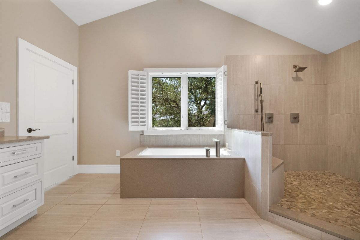 Bathroom with drop-in tub, large walk-in shower, and dual vanities. 