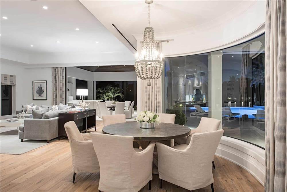 Round Dining Table with a Striking Poolside View and Statement Chandelier