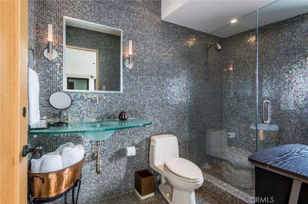 Full wall of reflective mosaic tile surrounds a compact bathroom layout.