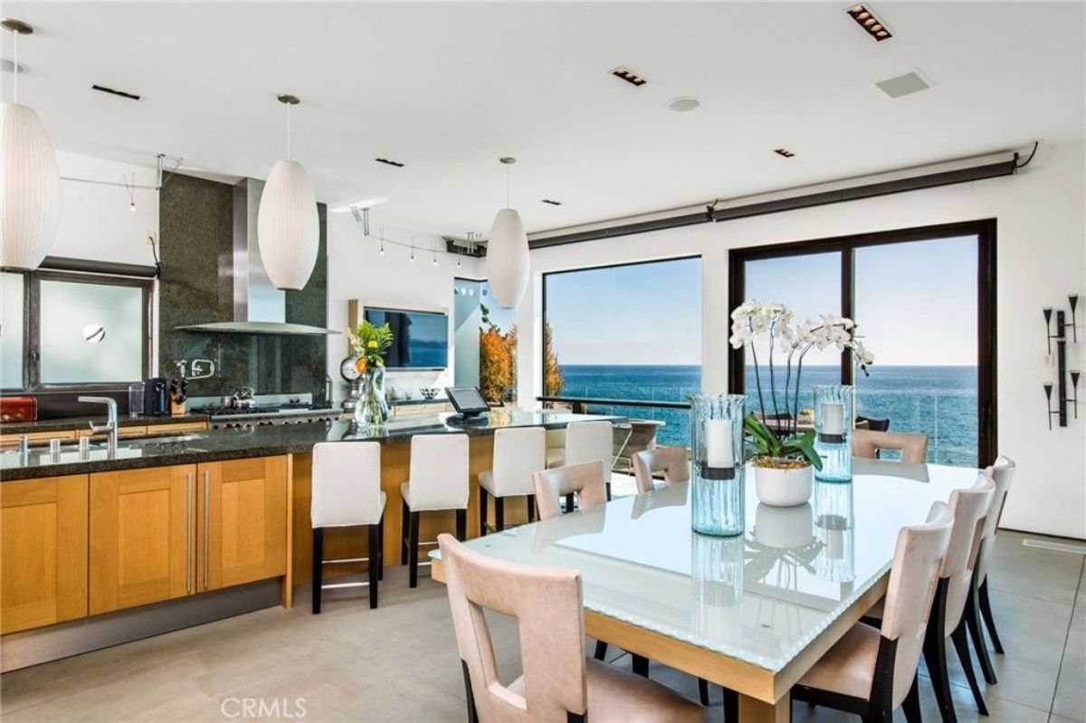Glass-top dining table and white chairs sit next to a long kitchen island with bar seating.