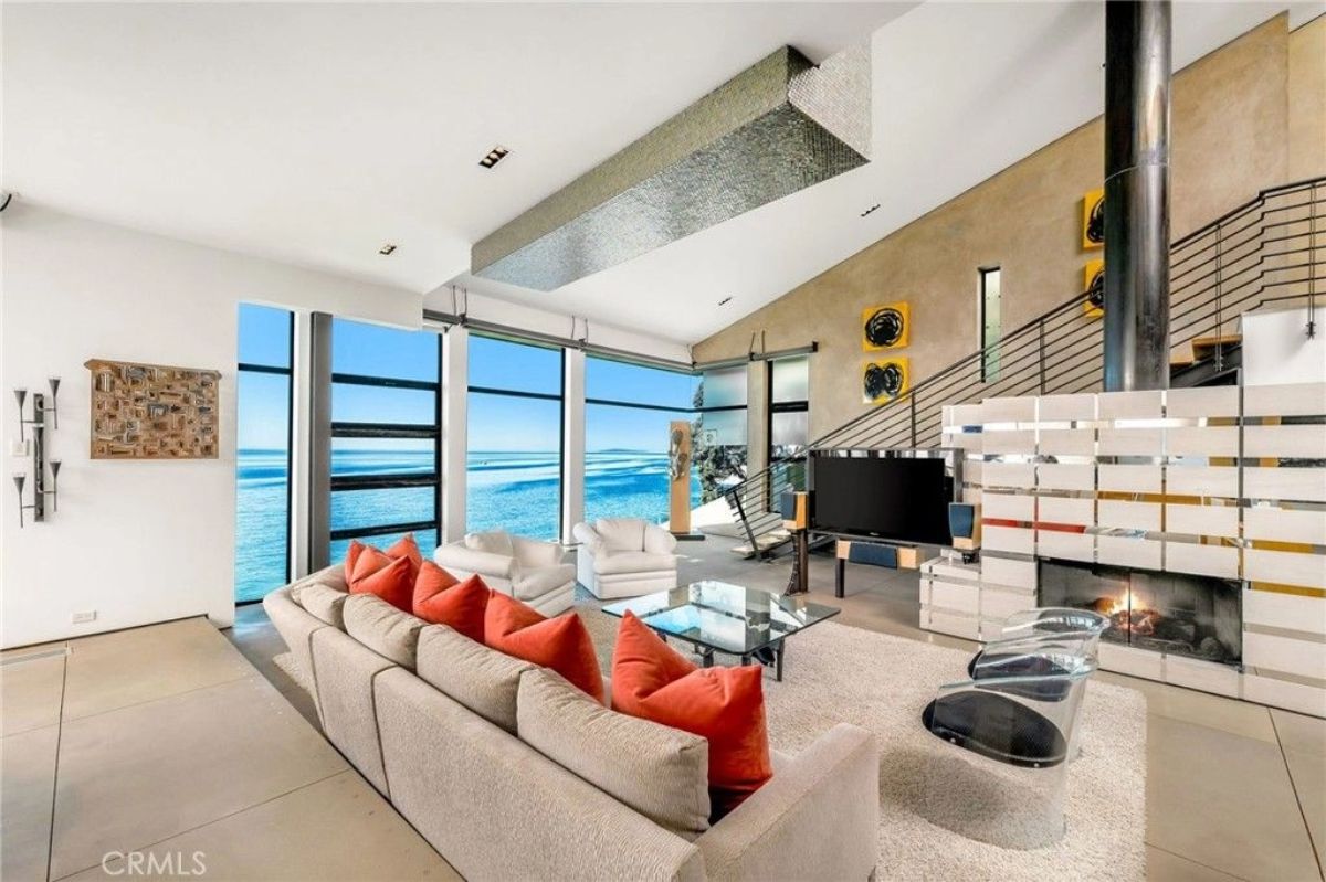 Floor-to-ceiling windows line the wall beside a sectional sofa with red pillows.