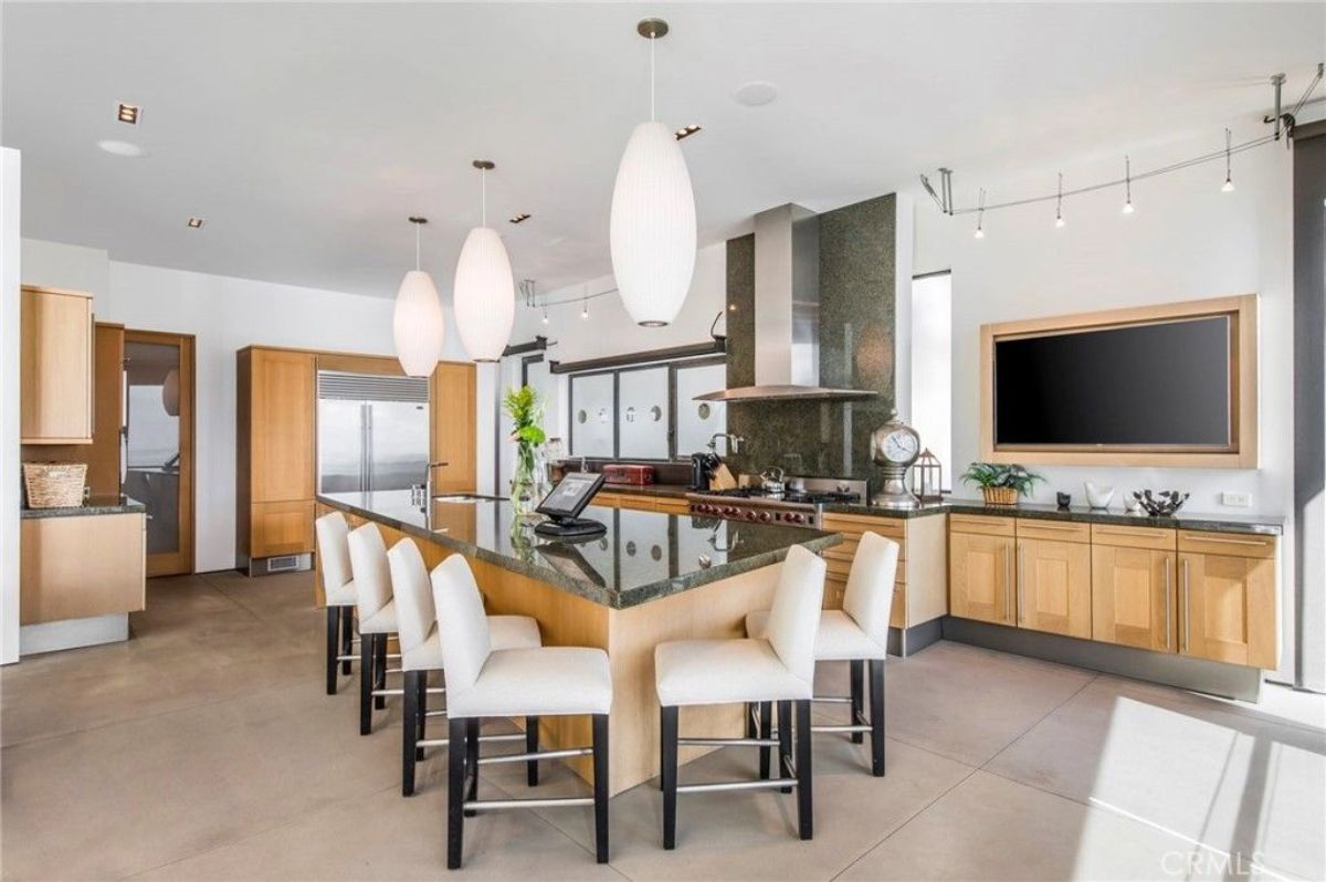 Barstools surround a wide island across from a media wall and prep counter.