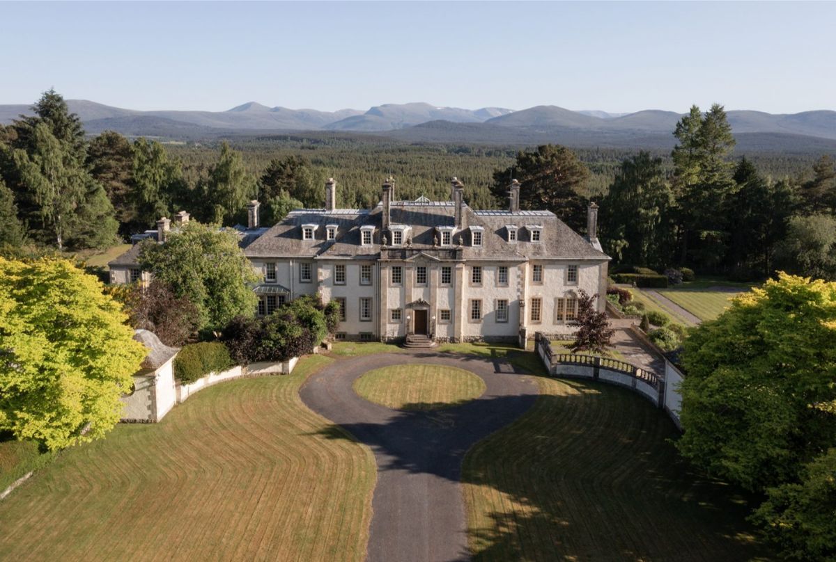 Symmetrical mansion sits at the center of a curved drive lined with manicured lawn.
