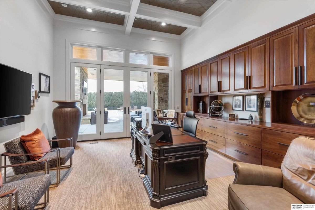Home office with coffered ceiling, built-in wood cabinetry, desk, and patio access.