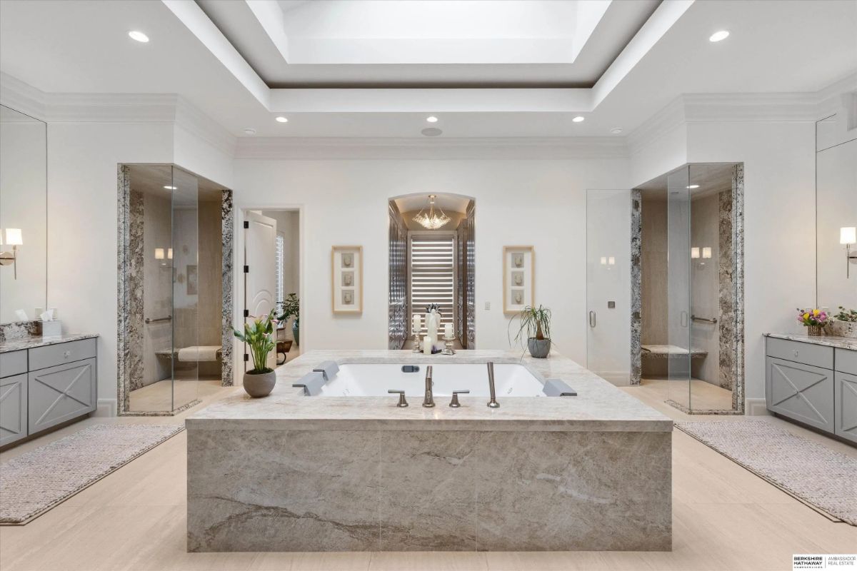 Bathroom with central soaking tub, dual vanities, marble surfaces, and skylight above.