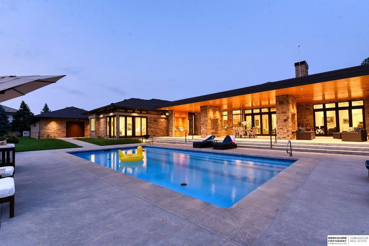 Swimming pool with concrete surround, lounge chairs, and full-width covered patio illuminated at dusk.