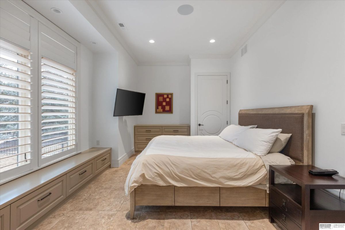 Guest bedroom with wall-mounted TV, built-in bench storage, and neutral tones throughout.