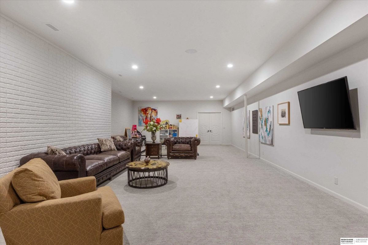 Basement lounge with sectional seating, flat-screen TV, white brick accent wall, and recessed lighting.