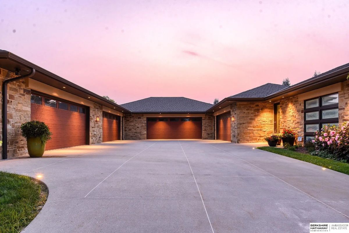 Multi-bay driveway with stone garage façades, recessed lighting, and curved layout at sunset.