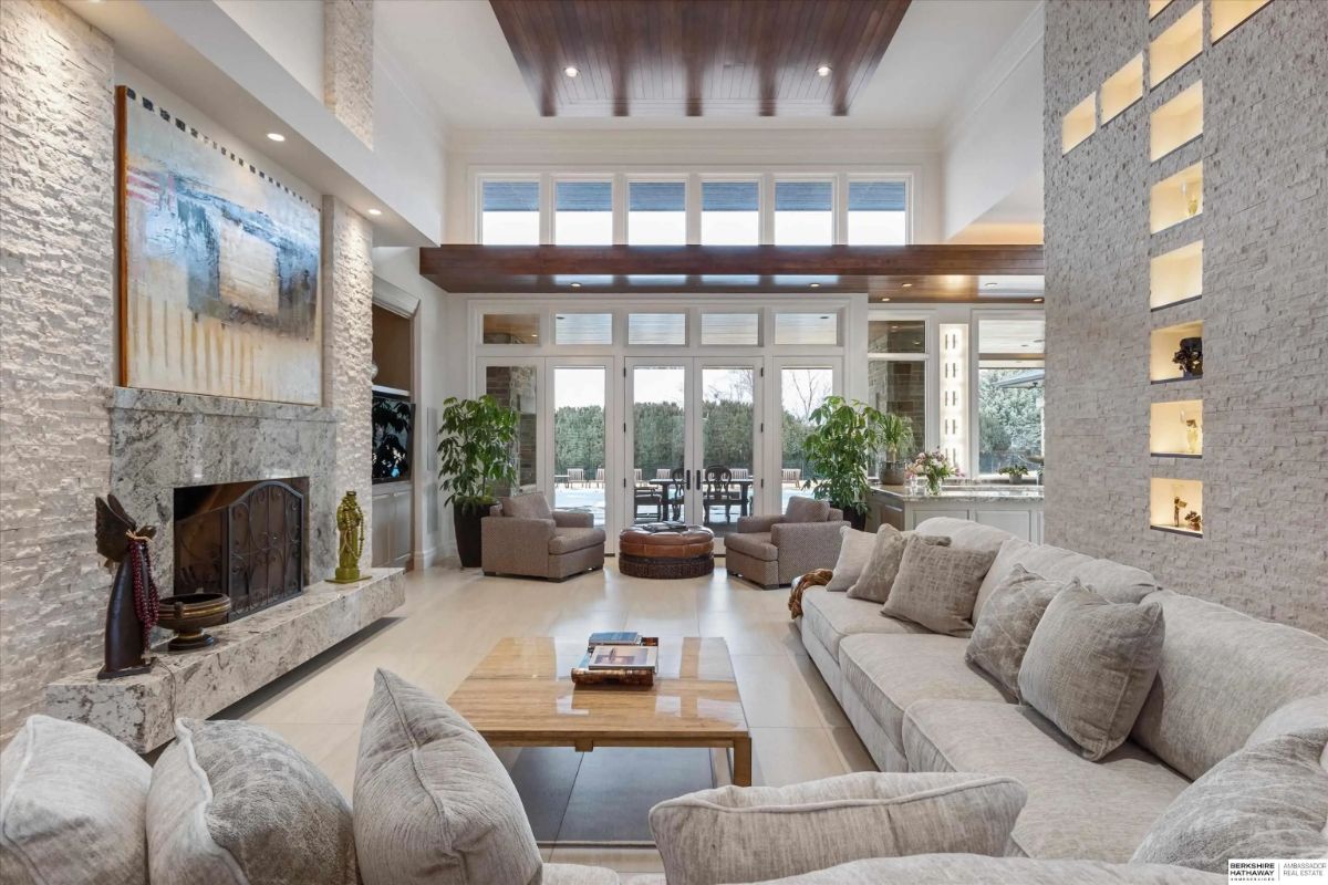 Living room with tall ceilings, stacked stone fireplace, floor-to-ceiling windows, and sectional seating.