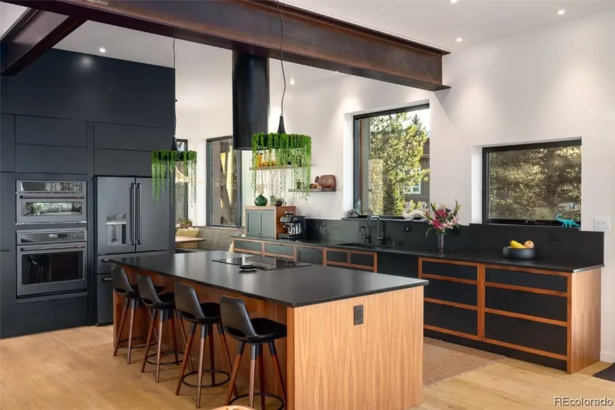 Kitchen with black countertops, wood cabinetry, and green glass pendant lights includes island seating for four.