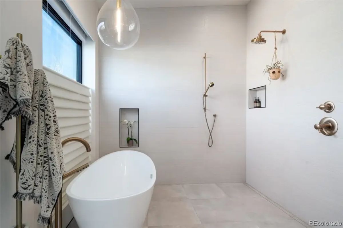 Minimalist wet room with freestanding oval tub, wall-mounted shower fixtures, and large window.