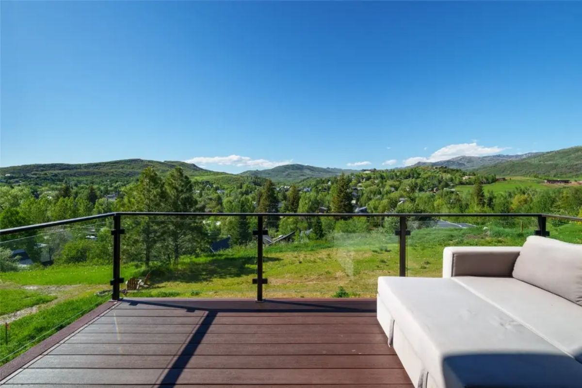 Outdoor deck with cushioned sectional sofa overlooks green valley and distant hills.