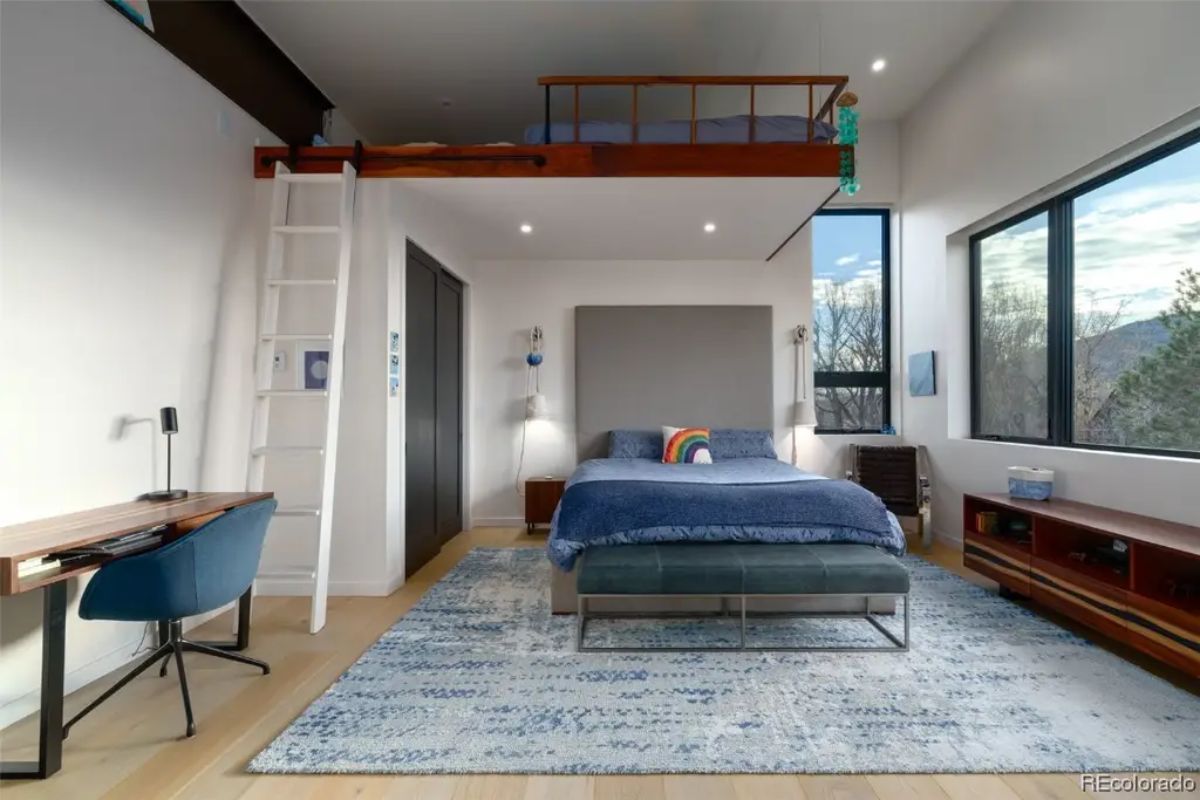 Bedroom with a loft, modern desk, large windows, and a bed on a blue-patterned area rug.
