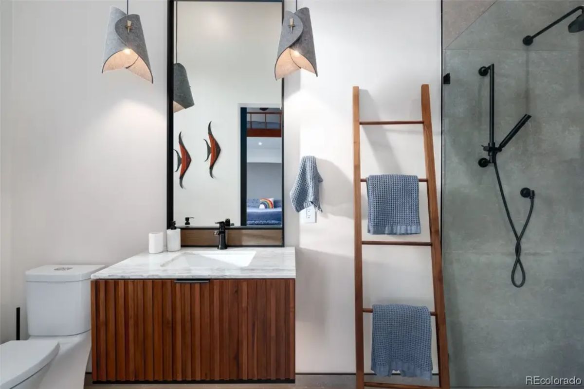 Bathroom with vertical wood-slat vanity, large mirror, towel ladder, and walk-in shower with black fixtures.