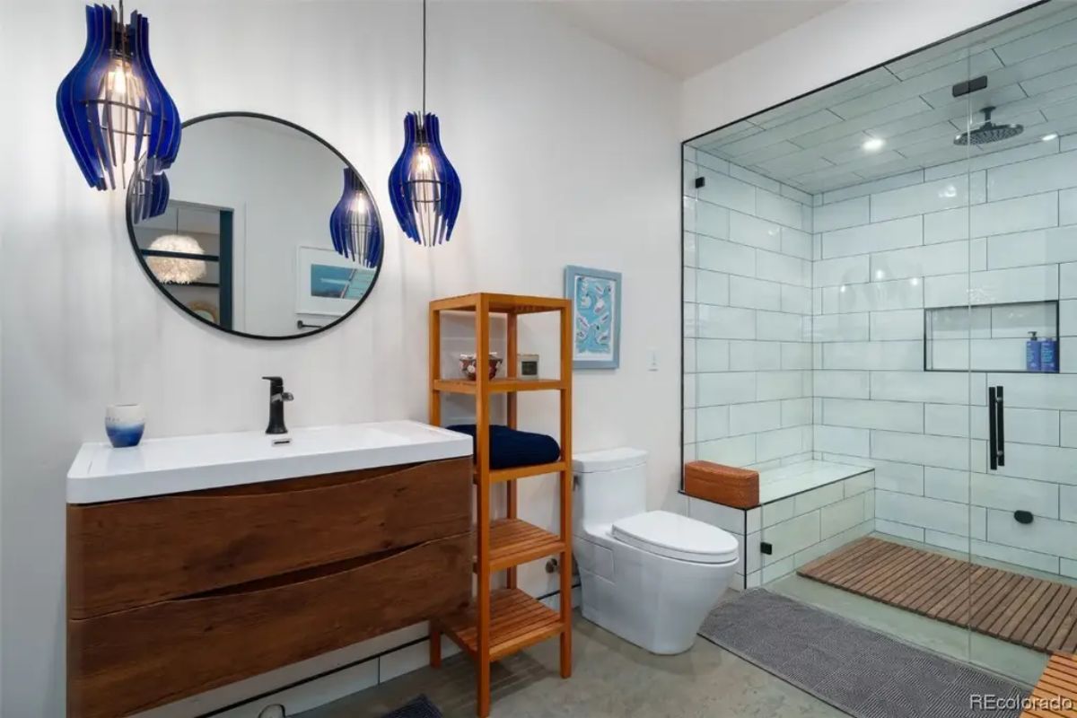 Bathroom with wood vanity, blue pendant lights, open shelving, and glass walk-in shower with rain head.