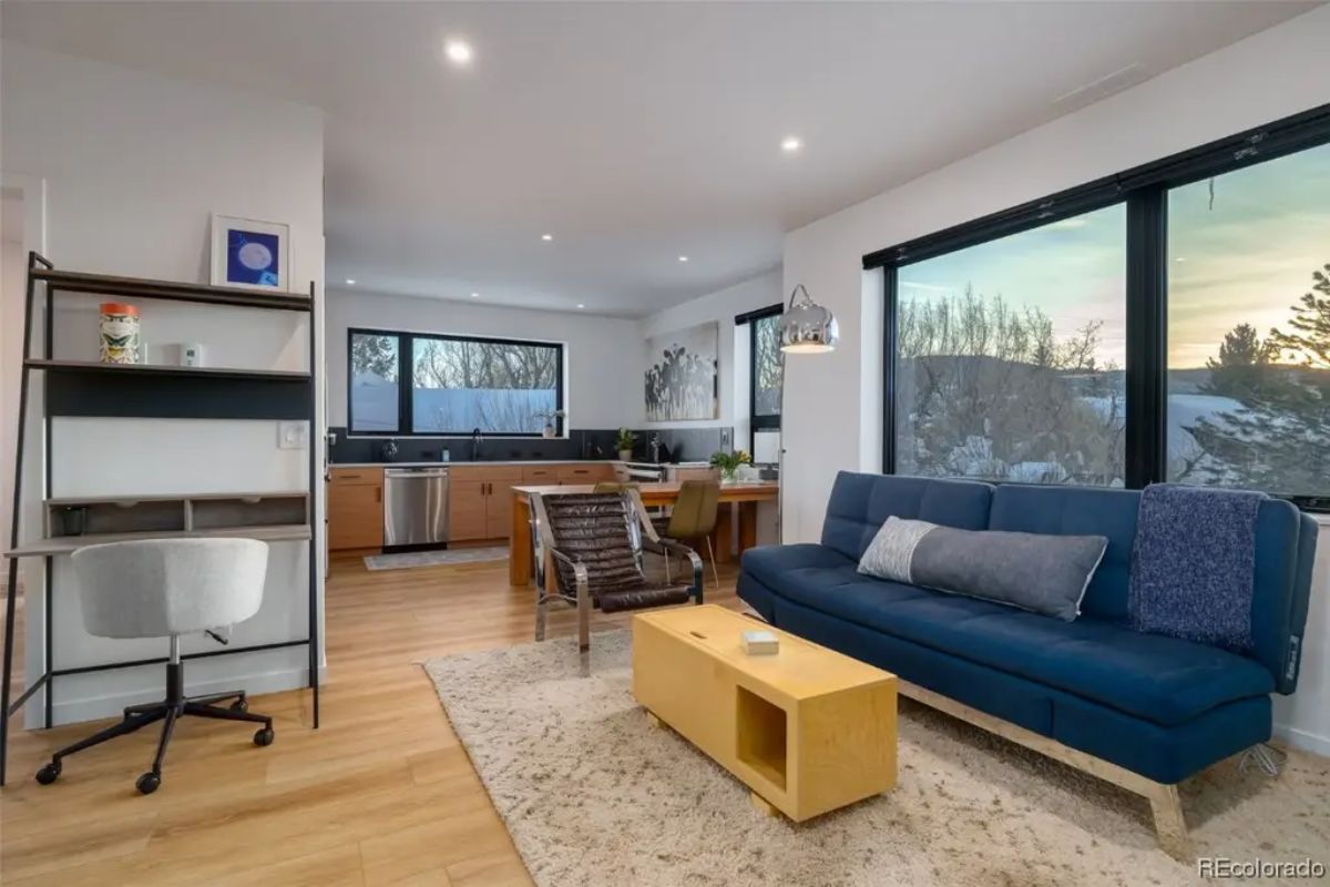 Open living and dining area with compact kitchen, navy loveseat, wood furniture, and large corner windows.