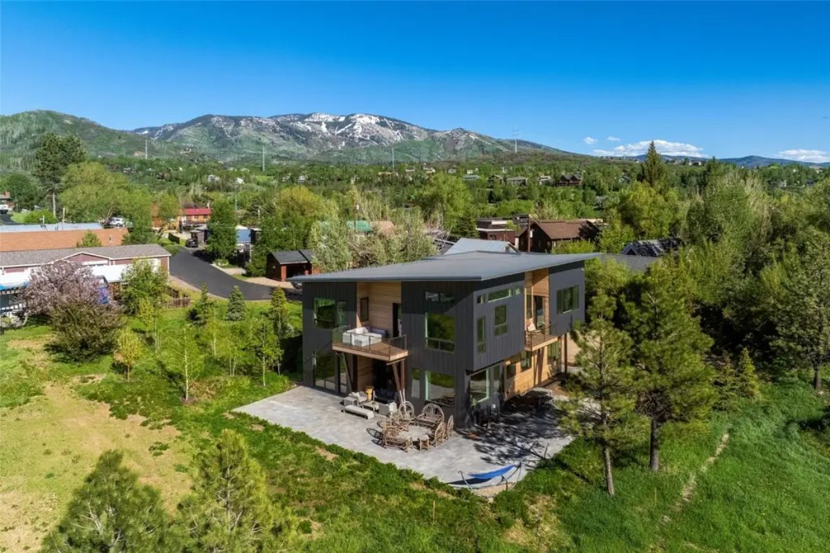 Contemporary home with extended patio sits among other houses with distant mountain views.