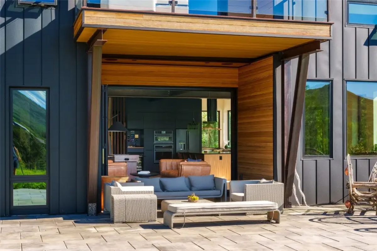 Patio area with cushioned outdoor seating opens to interior living space through wide retractable glass wall.