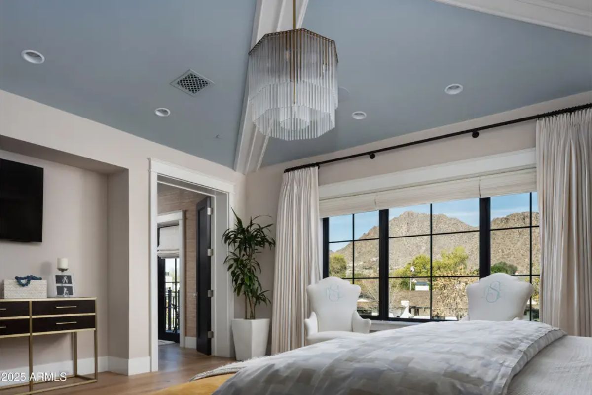 Bedroom with light blue tray ceiling, chandelier, and large window facing mountain views.