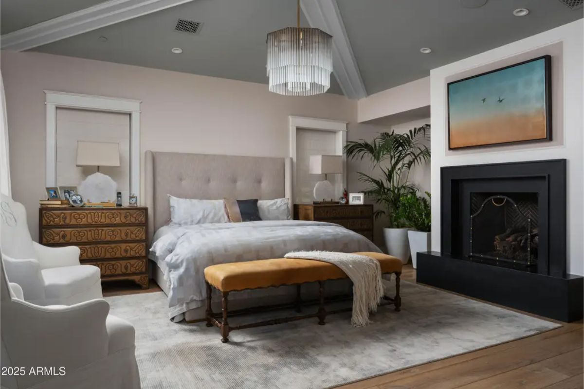 Bedroom with upholstered bed, fireplace, and wooden bench on a neutral area rug.