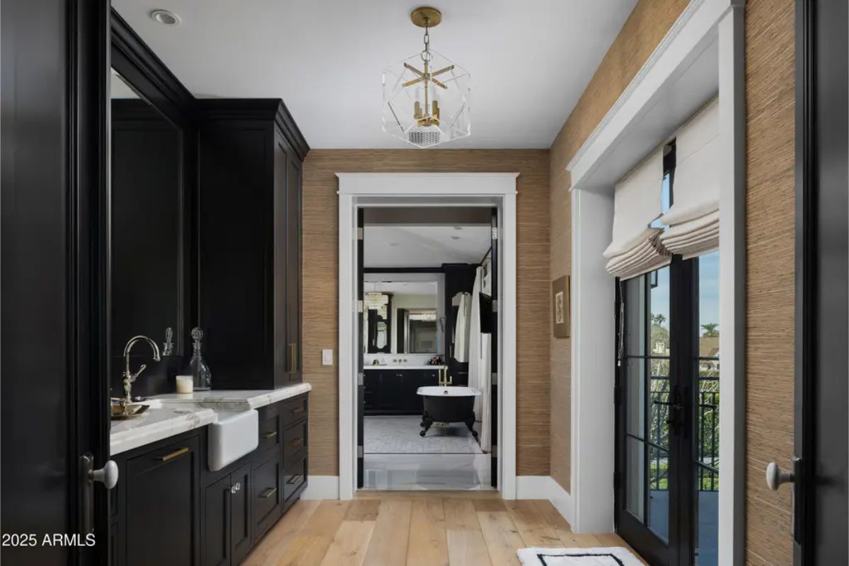 Vanity area with dark cabinetry, farmhouse sink, and view into a marble-floored bathroom.