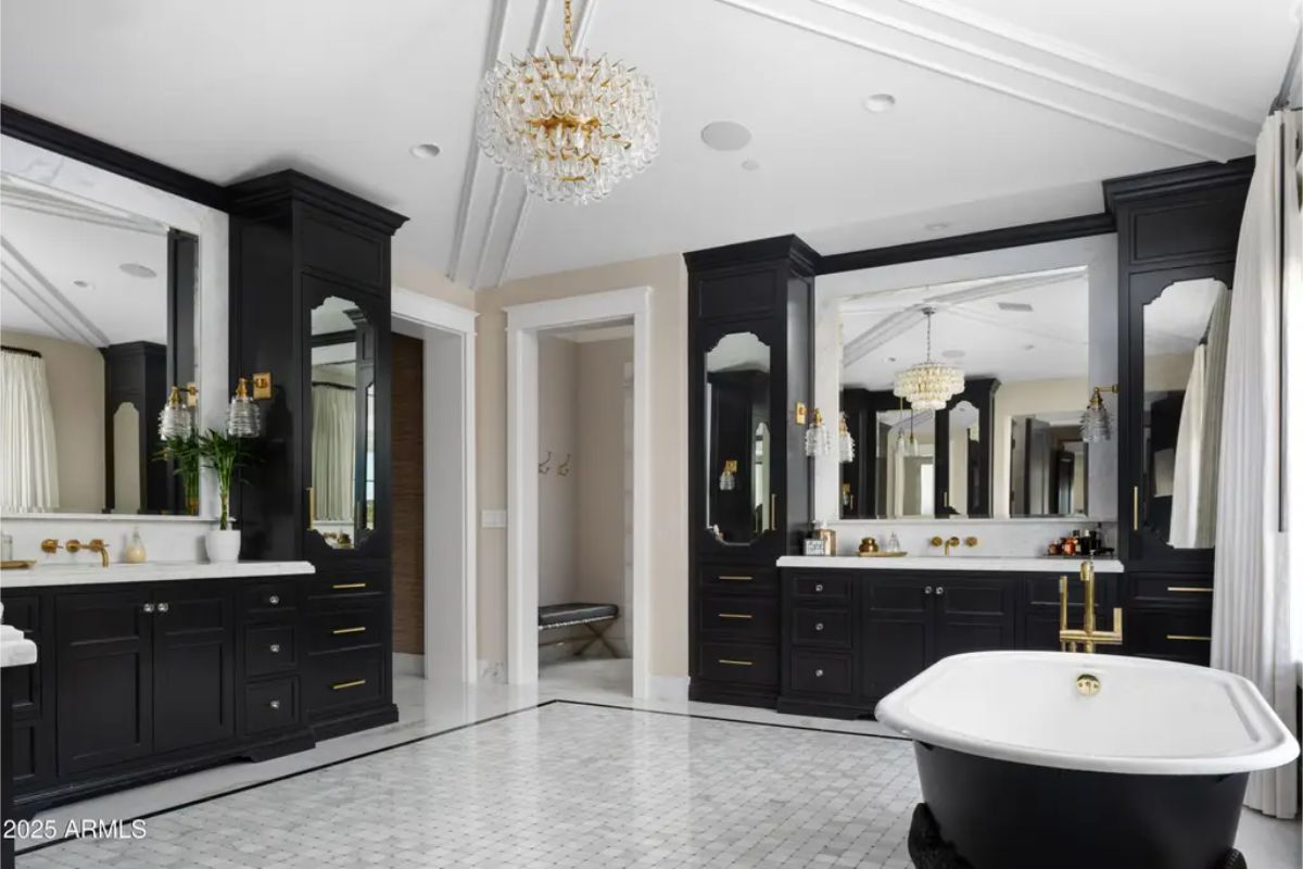 Bathroom with freestanding tub, dual vanities, chandeliers, and black cabinetry.