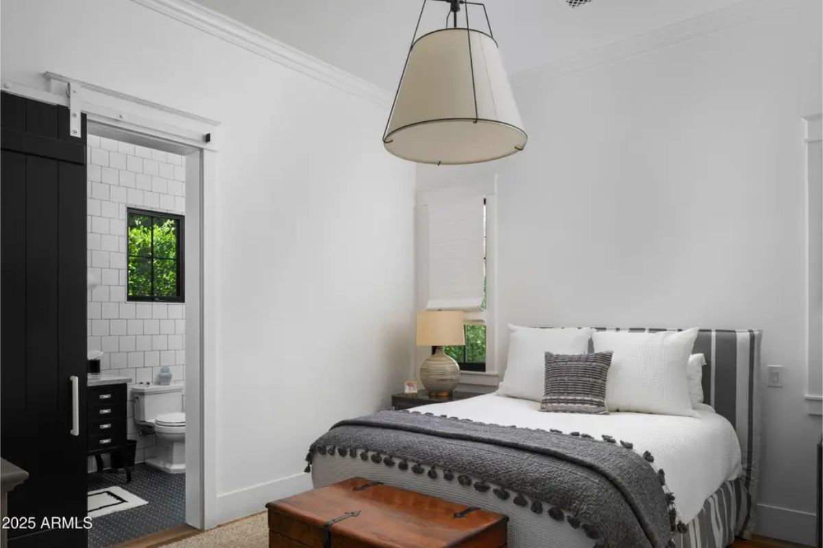 Compact bedroom with white walls, striped bedding, and attached bathroom with black and white tile.