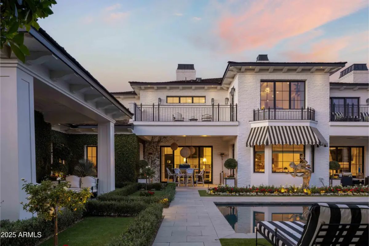 Closer view of the rear patio with covered seating, manicured landscaping, and balcony above.