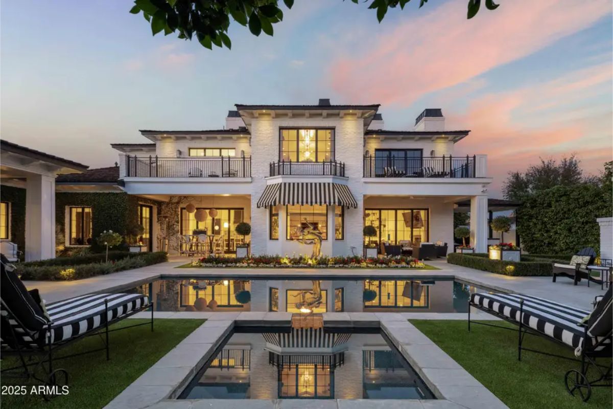 Rear exterior of white two-story home with striped awnings, reflecting pool, and lounge seating.