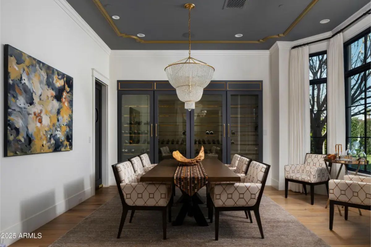 Formal dining room with chandelier, upholstered chairs, and wine storage behind glass doors.