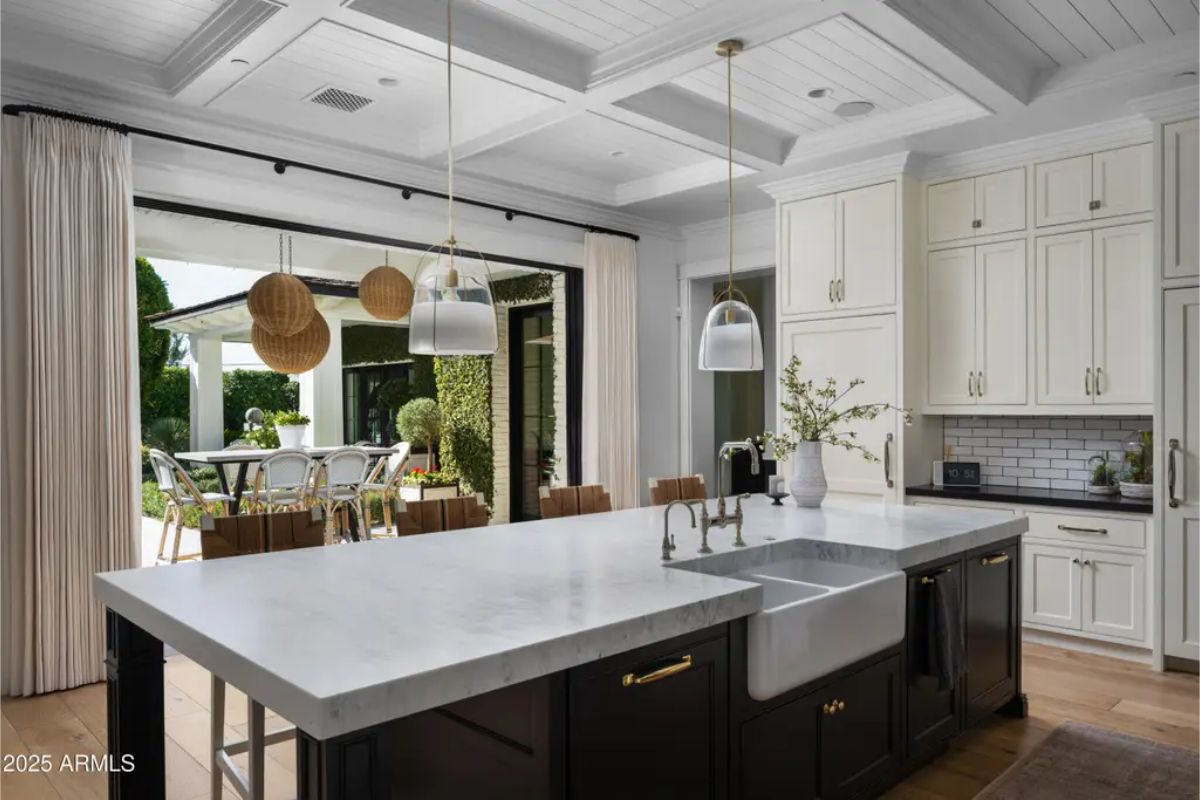 Kitchen with black island, white countertops, farmhouse sink, and open view to patio dining area.
