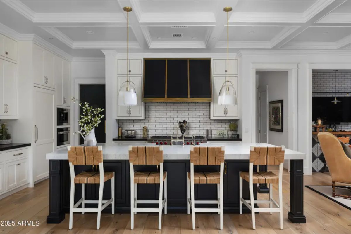 Kitchen with black and white island, pendant lights, and built-in range with white cabinetry.