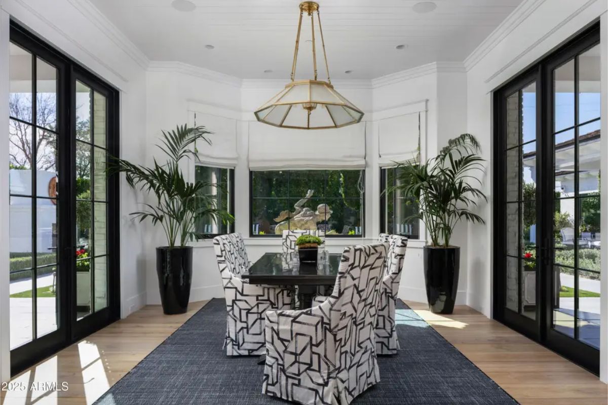 Breakfast room with large windows, geometric-print chairs, and black dining table.