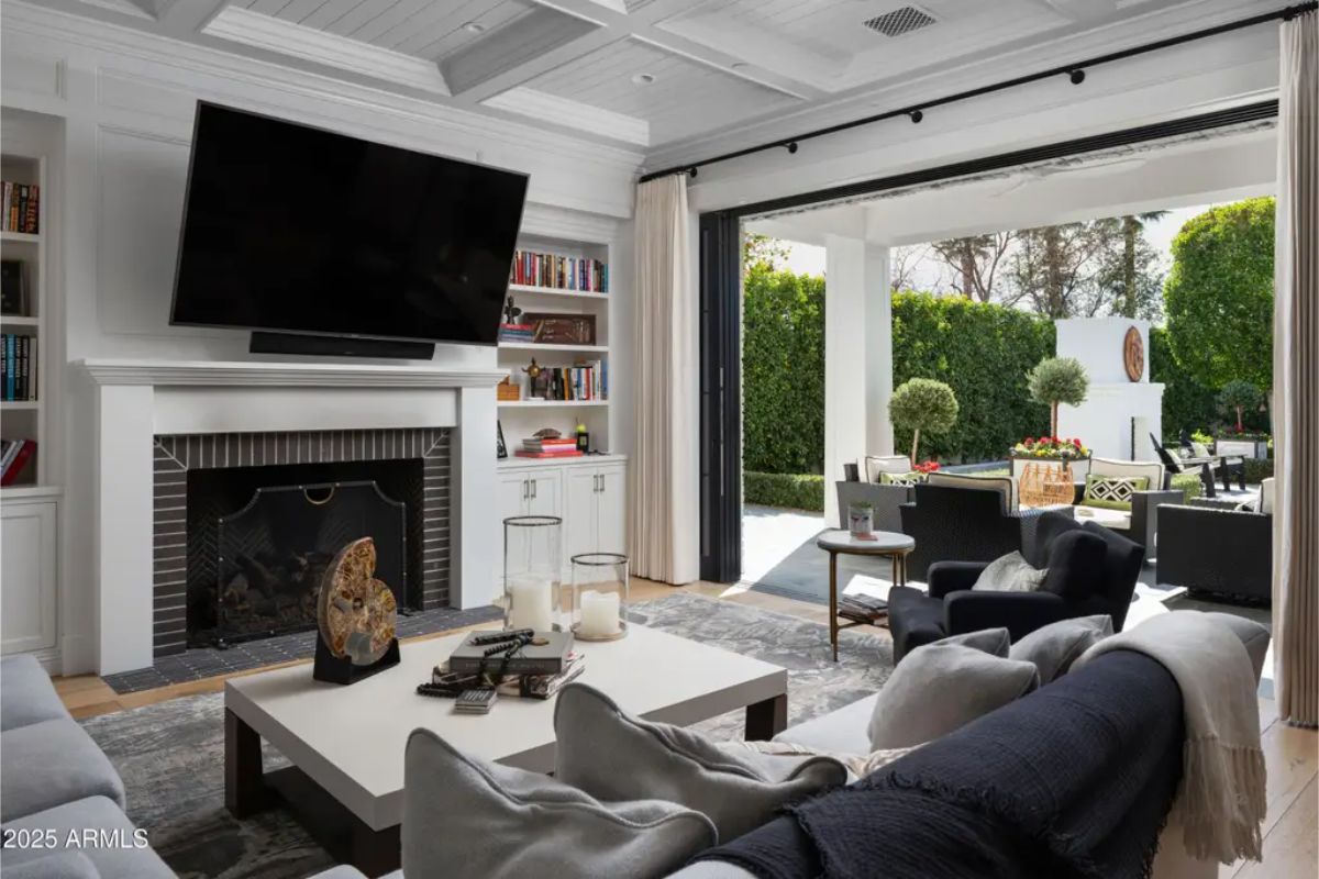 Living room with large TV above a fireplace, built-in shelving, and folding glass doors opening to a patio. 