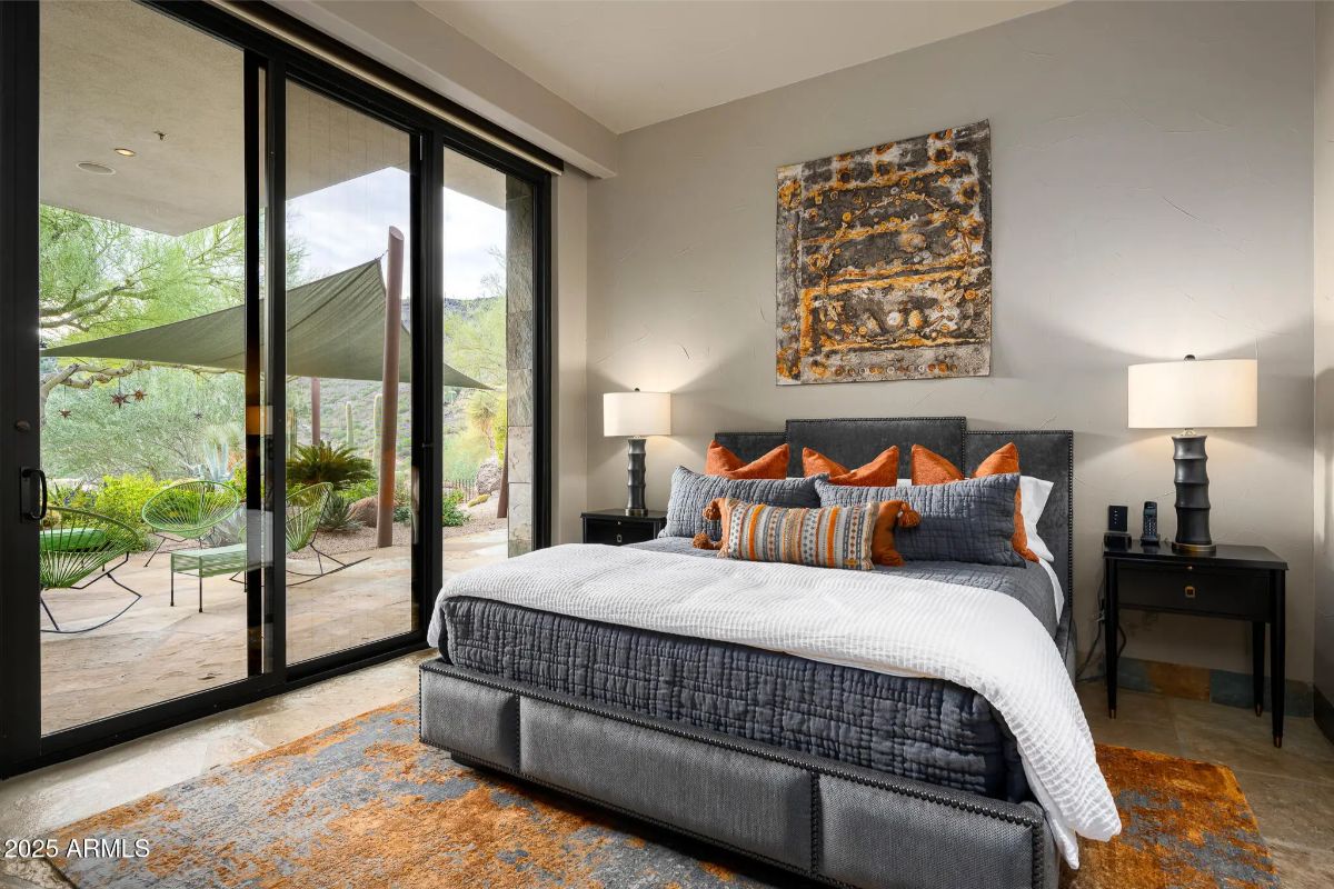 Bedroom with textured wall art, orange accent pillows, and floor-to-ceiling sliding doors facing shaded outdoor seating.