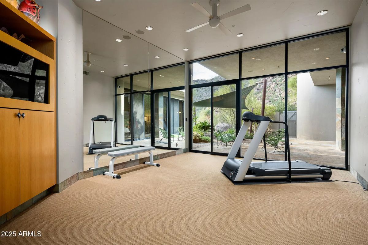 Fitness room with treadmill, weight bench, and floor-to-ceiling windows overlooking courtyard.