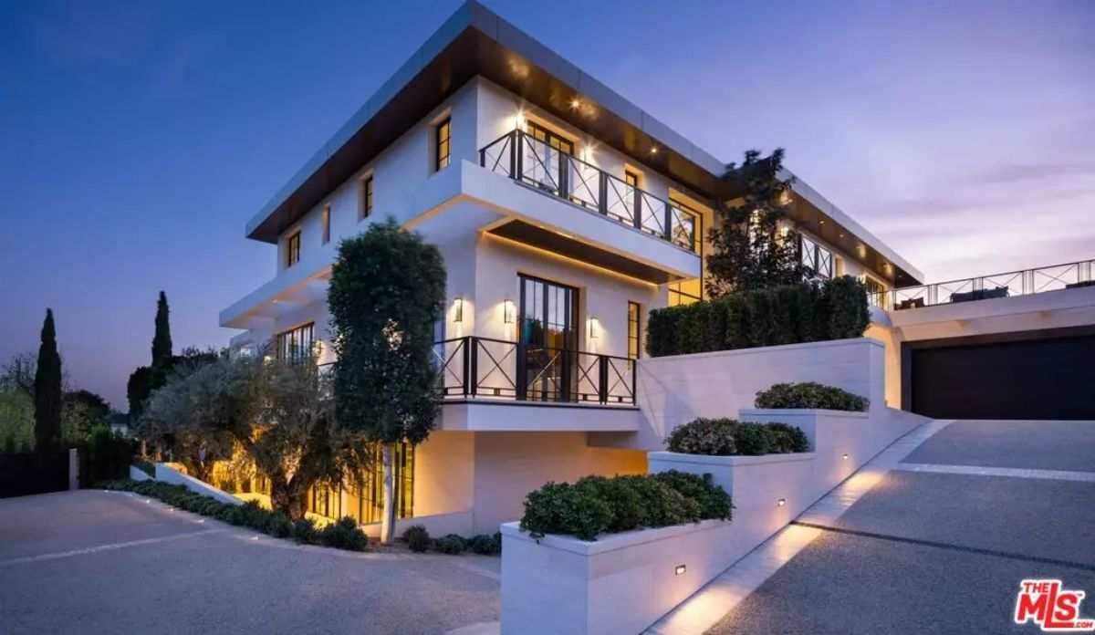 Multi-level residence at twilight with lit landscaping, wraparound balconies, and sloped driveway.