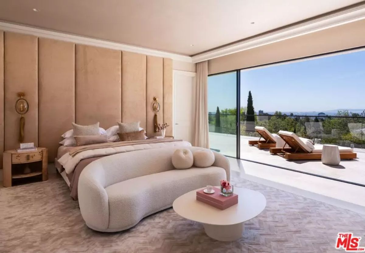 Bedroom with curved sofa and wall-panel headboard opens to outdoor terrace with lounge chairs.
