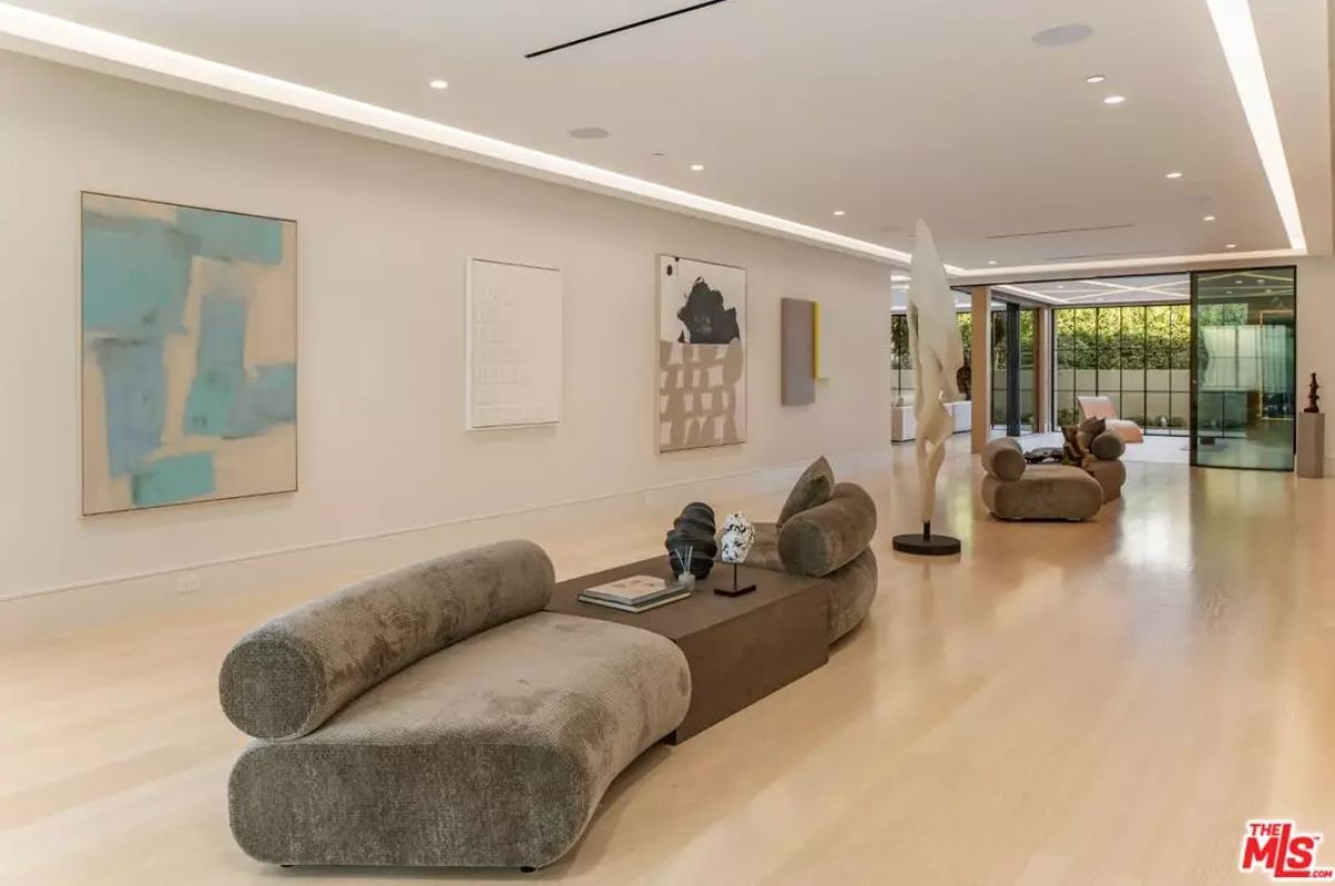 Hallway with light wood flooring, sculptural furniture, and abstract artwork leads to glass doors.