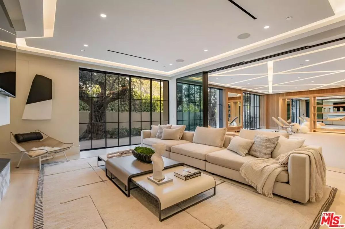 Living room with beige sectional, modern decor, and floor-to-ceiling glass walls opening to patio.
