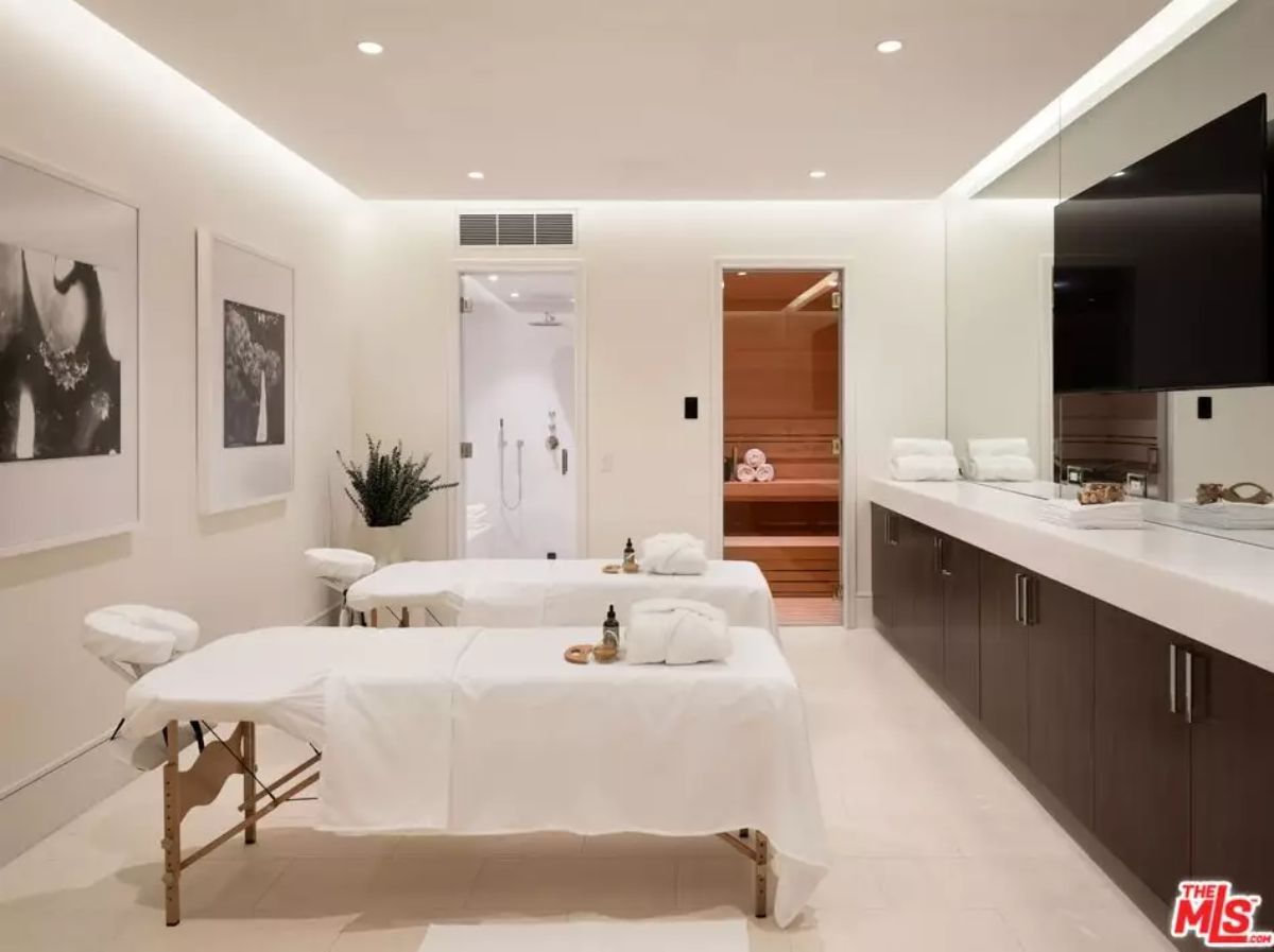 Spa room with dual massage tables, long vanity, and sauna room in the background.