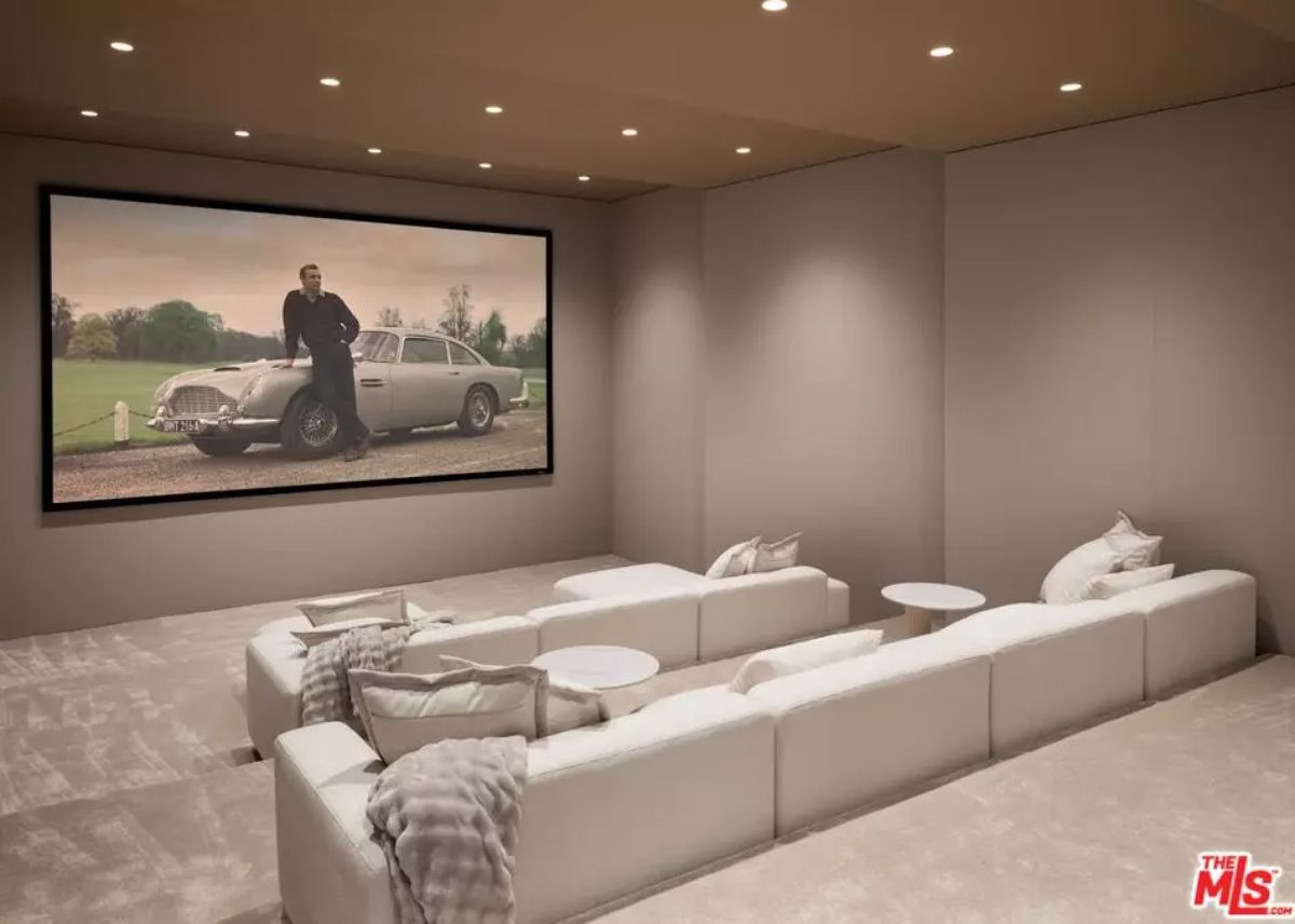 Home theater with tiered white sectionals and large wall screen surrounded by recessed lighting.