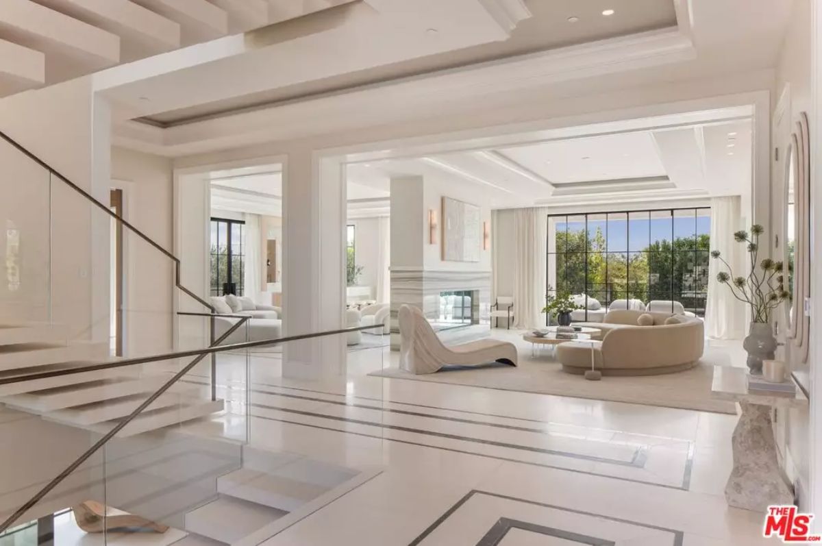 Open interior with white marble flooring, glass staircase, and multiple sitting areas facing large windows.