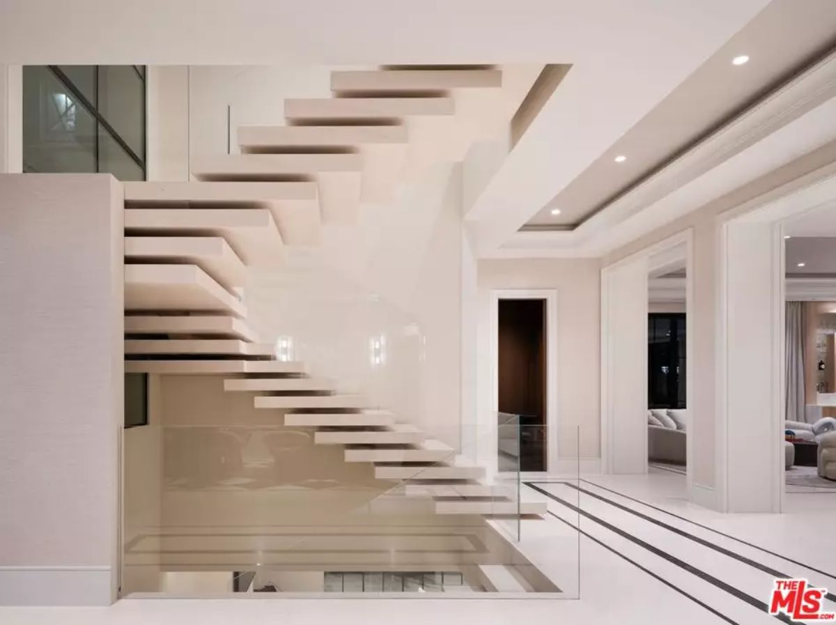 Floating staircase with white treads and glass railing spans three levels of an open-plan interior.