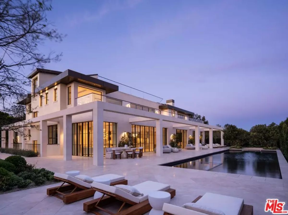 Rear view of large contemporary home with multiple patios, loungers, and lap pool along tiled terrace.