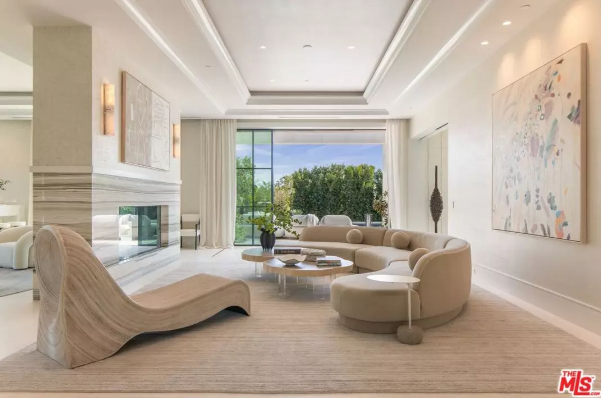Lounge with curved sofa, modern chaise, fireplace, and sliding doors opening to hedge-lined yard.